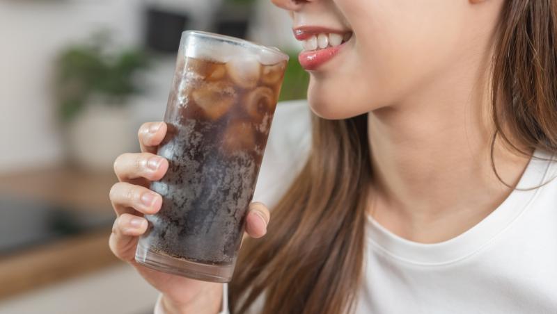 Tânără însetată care bea, ținând un pahar cu apă rece cu gheață în mână