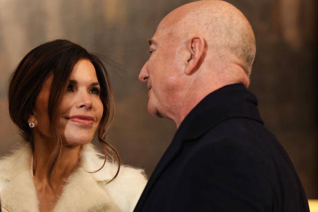 Jeff Bezos îmbrăcat într-un costum negru, alături de Lauren Sanchez, îmbrăcată într-o haină bej pufoasă