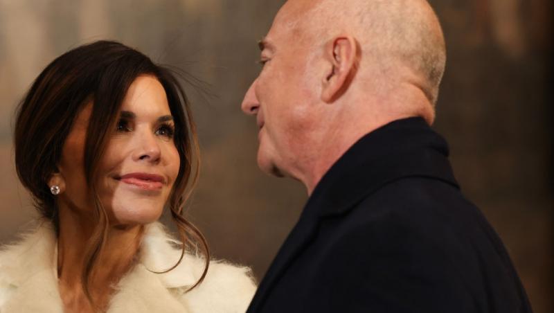 Jeff Bezos îmbrăcat într-un costum negru, alături de Lauren Sanchez, îmbrăcată într-o haină bej pufoasă
