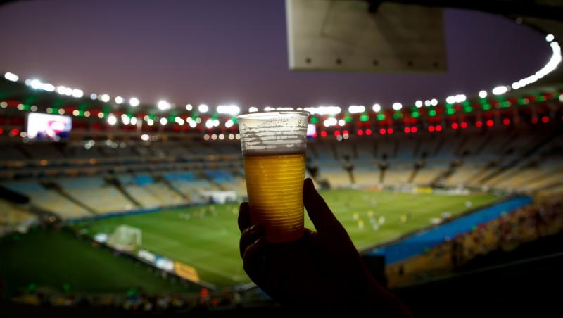 Un pahar de bere fotografiat la înățime din tribuna unui stadion