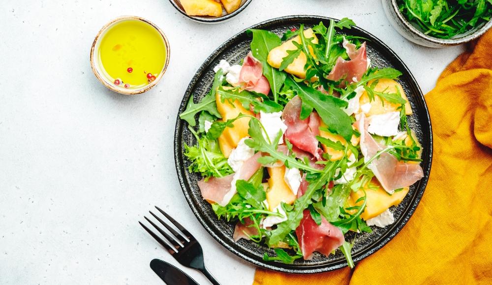 Salată cu pepene galben, prosciutto și mozzarella pe o farfurie neagră