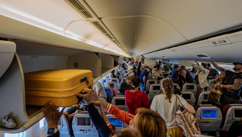 imagine cu multi oameni in avion care stau in picioare si isi iau bagajele