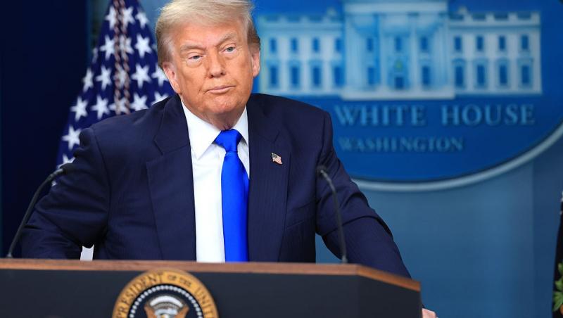 Donald Trump îmbrăcat cu un costum bleumarin și o cravată albastră, vorbind la microfon