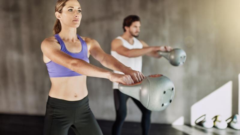 femeie și bărbat în sala de fitness care fac un exercițiu de balansare cu kettlebell
