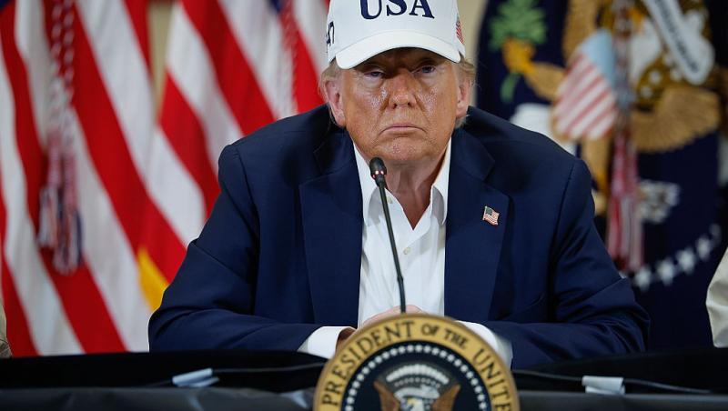 Donald Trump îmbrăcat cu un costum bleumarin, purtând o șapcă albă