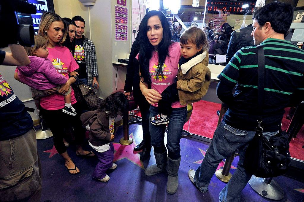 Nadya Suleman îmbrăcată cu un tricou roz și pantaloni din denim, înconjurată de copii