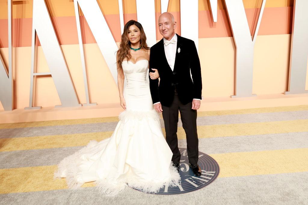 Jeff Bezos îmbrăcat în negru, alături de Lauren Sanchez, îmbrăcată în alb
