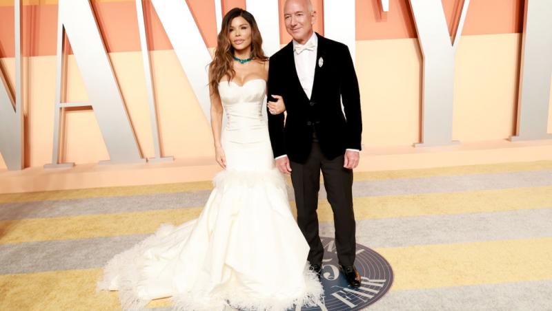Jeff Bezos îmbrăcat în negru, alături de Lauren Sanchez, îmbrăcată în alb