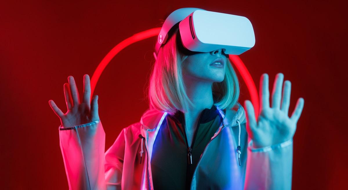 Femeie blondă cu o cască de realitate virtuală pe ochi, pe fundal roșu, pentru a ilustra inteligența artificială la concursul de Miss