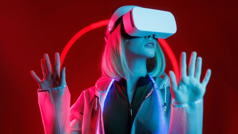 Femeie blondă cu o cască de realitate virtuală pe ochi, pe fundal roșu, pentru a ilustra inteligența artificială la concursul de Miss