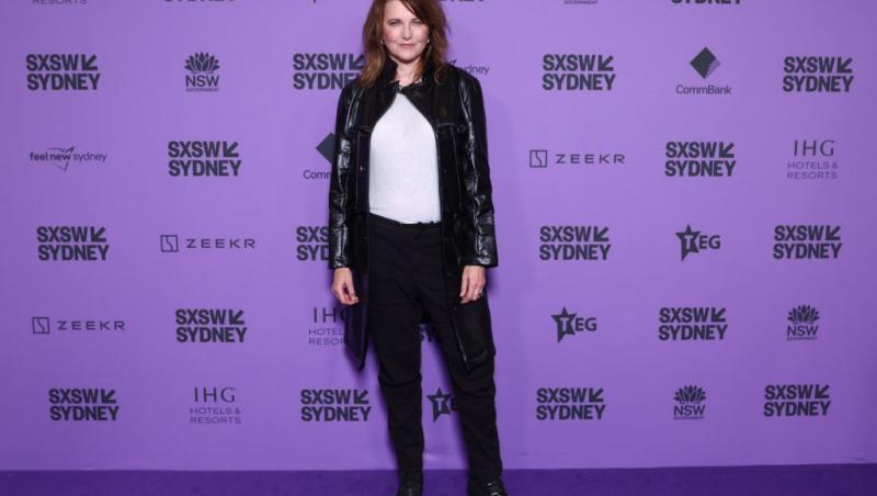Lucy Lawless îmbrăcată cu o jachetă neagră din piele, peste o bluză albă
