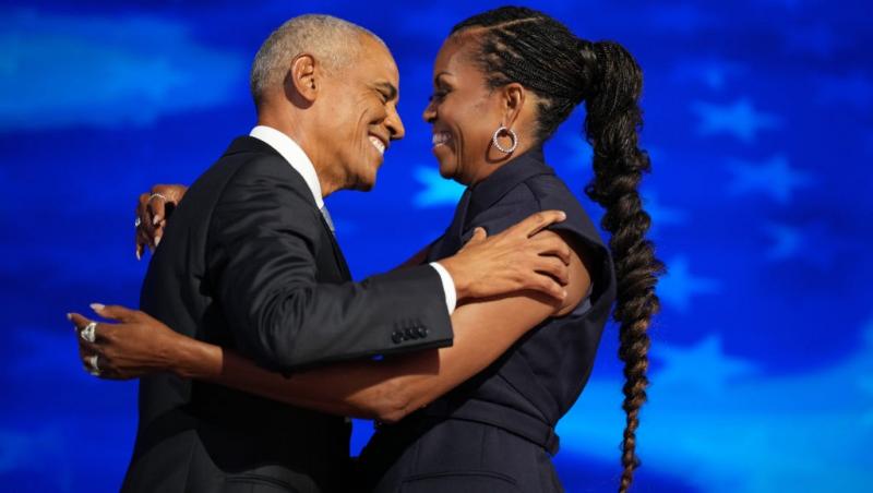 Barack Obama îmbrăcat într-un costum negru îmbrățișând-o pe soția lui, Michelle Obama, îmbrăcată într-o rochie neagră