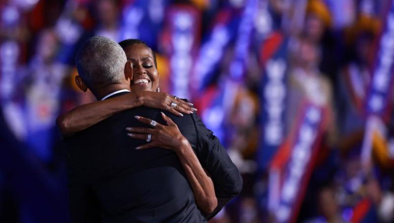 Barack Obama îmbrăcat într-un costum negru îmbrățișând-o pe soția lui, Michelle Obama, îmbrăcată într-o rochie neagră
