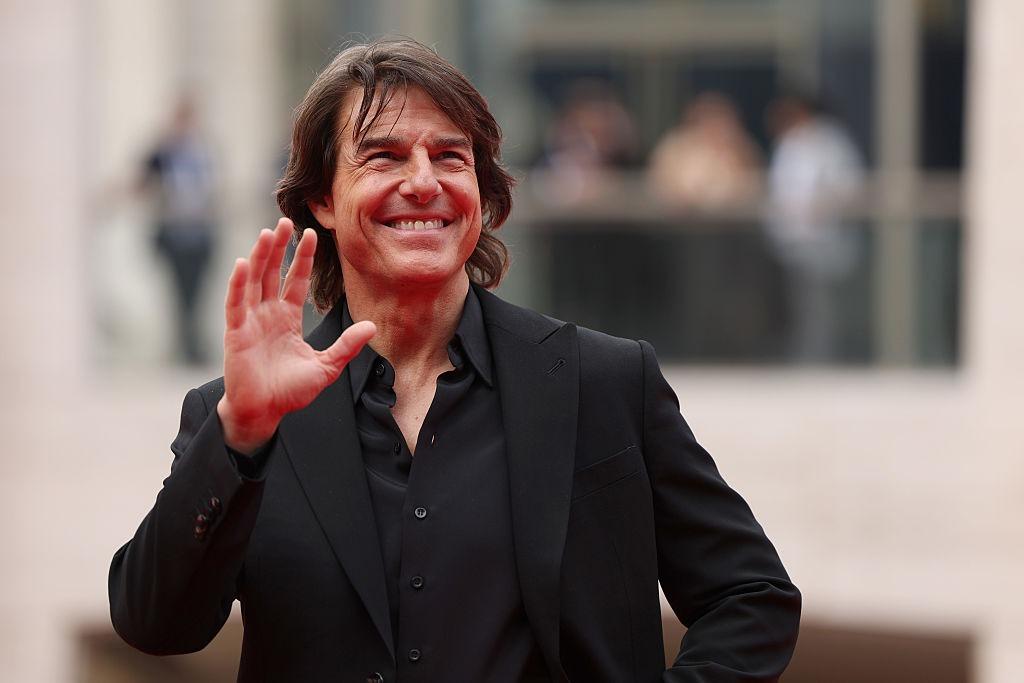 Tom Cruise îmbrăcat cu un costum negru și o cămașă neagră, salutând lumea