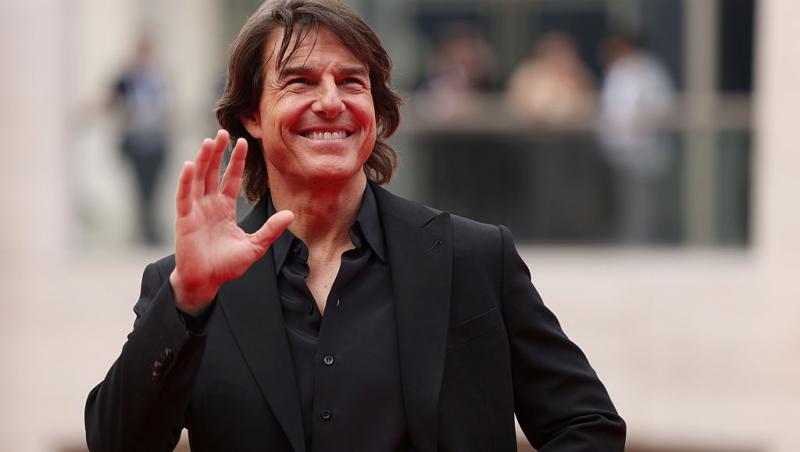 Tom Cruise îmbrăcat cu un costum negru și o cămașă neagră, salutând lumea