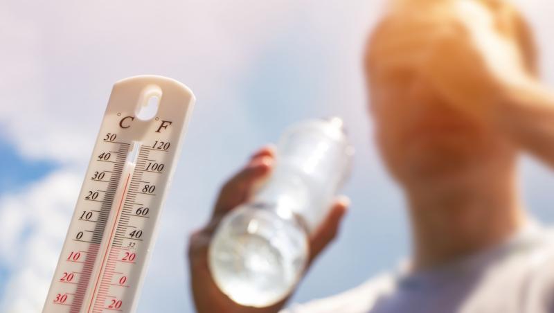 Bărbat care bea apă în căldură extremă și un termometru care indică un grad ridicat de temperatură cu soarele în fundal
