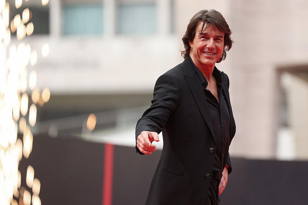 Tom Cruise îmbrăcat cu un costum negru și o cămașă neagră, salutând lumea