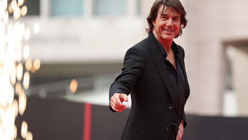 Tom Cruise îmbrăcat cu un costum negru și o cămașă neagră, salutând lumea