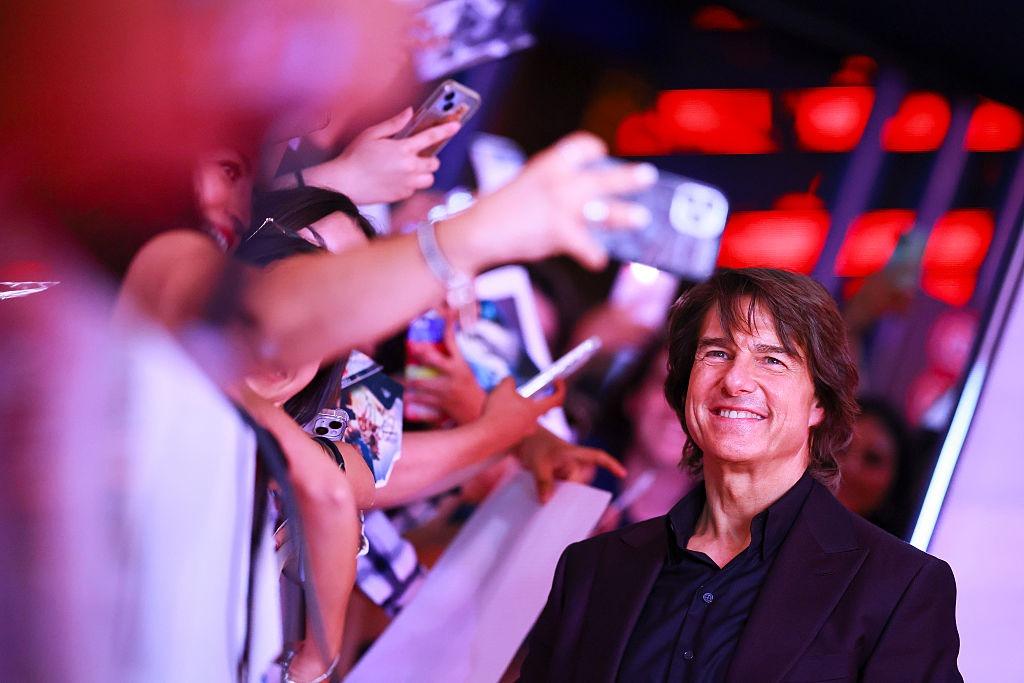 Tom Cruise îmbrăcat cu un costum negru și o cămașă neagră, mergând pe lângă fani