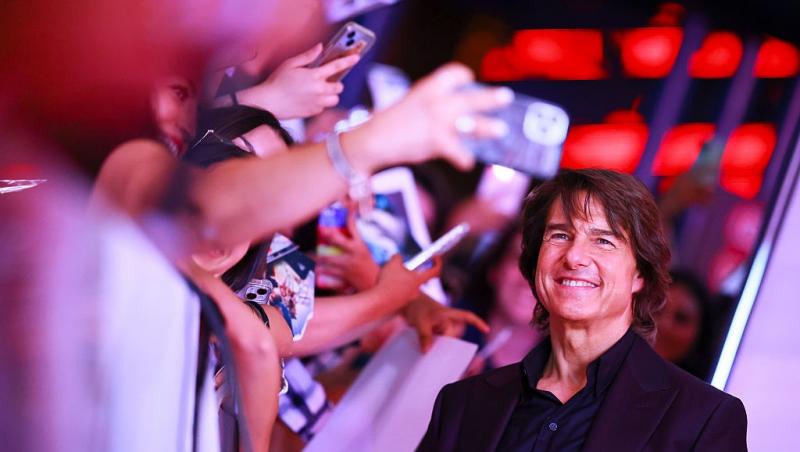 Tom Cruise îmbrăcat cu un costum negru și o cămașă neagră, mergând pe lângă fani