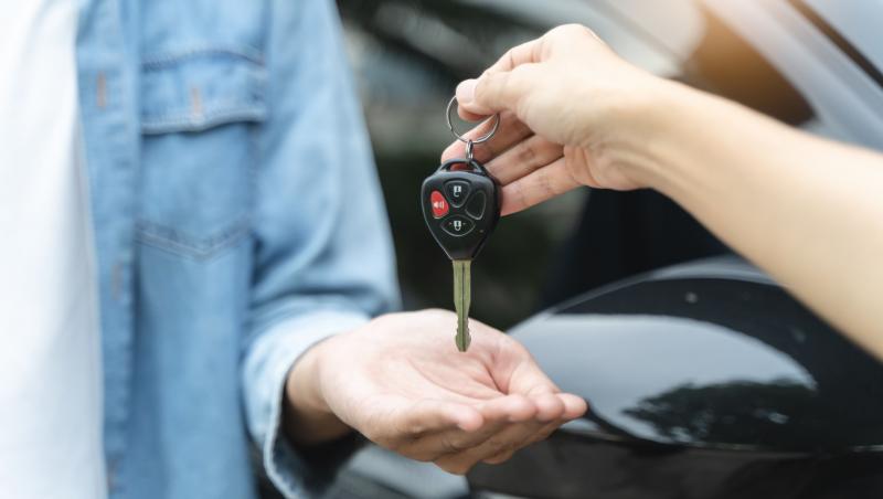 Mâna unui agent de mașini second-hand care dă o cheie unui cumpărător.