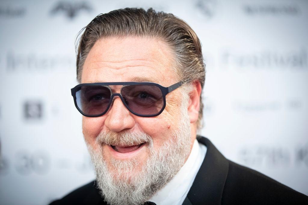 Russell Crowe îmbrăcat într-un costum negru, accesorizat cu ochelari de soare