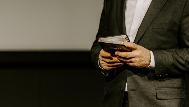 imagine cu un barbat cu costum si camasa care tine o biblie în mana