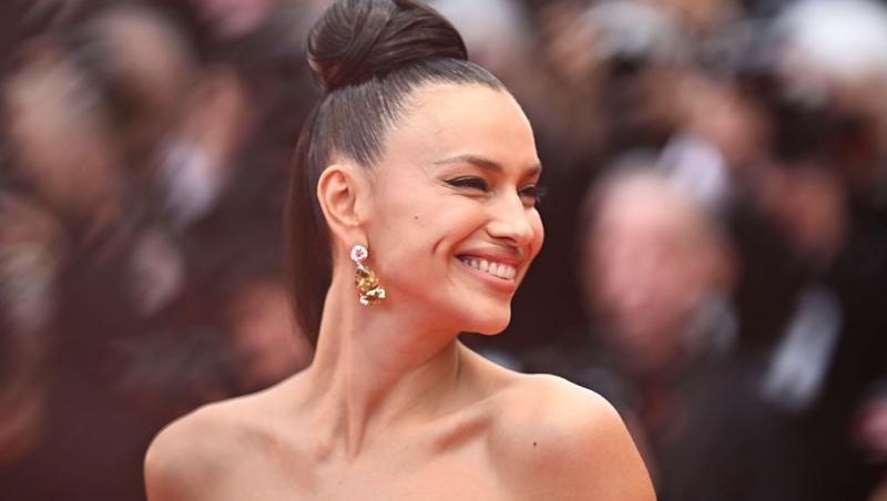 Irina Shayk îmbrăcată într-o rochie elegantă fără mâneci, zâmbind fericită