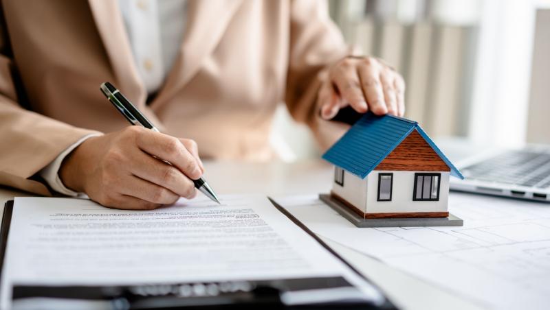 O clientă semnează Polița PAD și ține mâna cealaltă pe o casă în miniatură