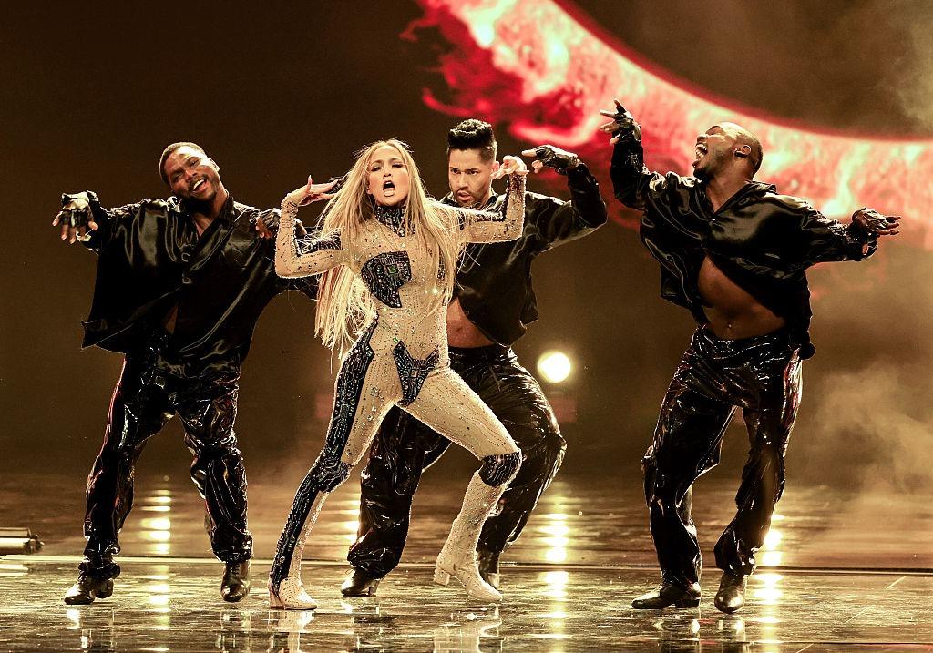 Jennifer Lopez îmbrăcată cu o ținută strălucitoare, dansând pe scenă cu echipa ei