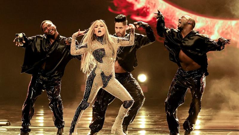 Jennifer Lopez îmbrăcată cu o ținută strălucitoare, dansând pe scenă cu echipa ei