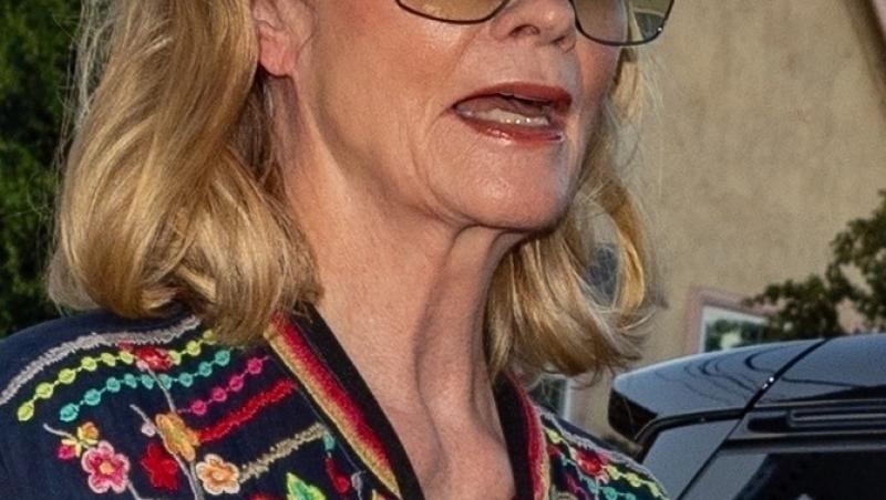 Cybill Shepherd îmbrăcată cu o bluză bleumarin cu detalii florale și pantaloni din denim