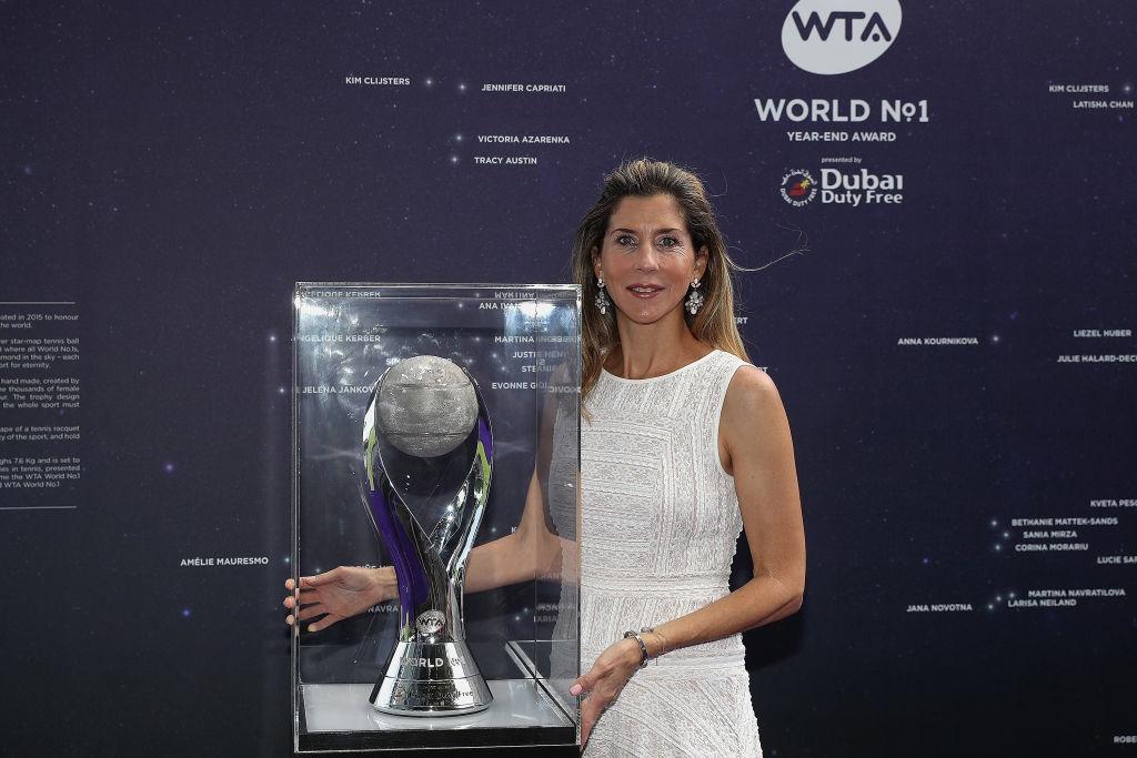 Monica Seles îmbrăcată cu o rochie albă, fără mâneci, pozând cu un trofeu
