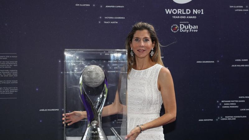 Monica Seles îmbrăcată cu o rochie albă, fără mâneci, pozând cu un trofeu