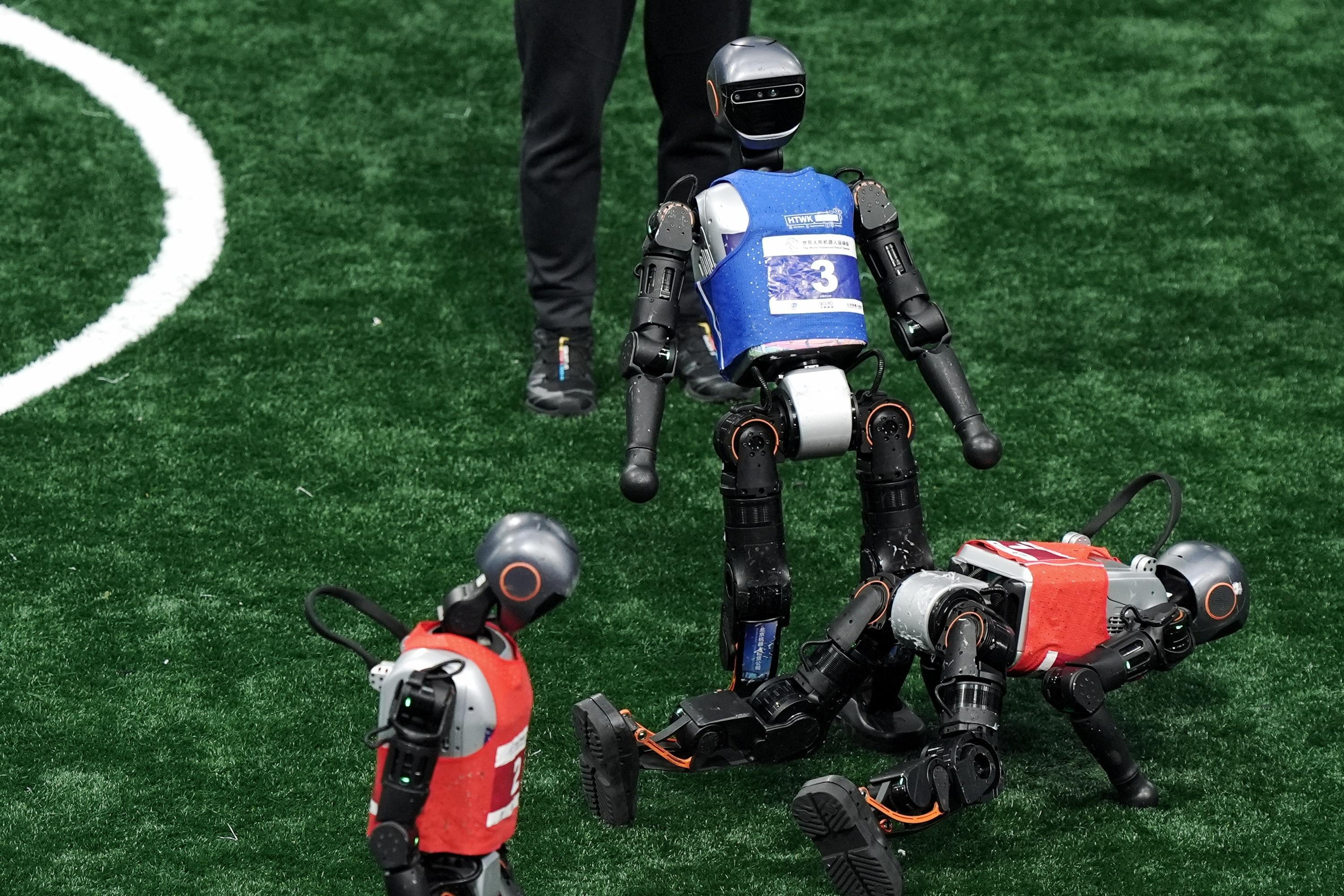 3 roboți care se află pe un teren de fotbal