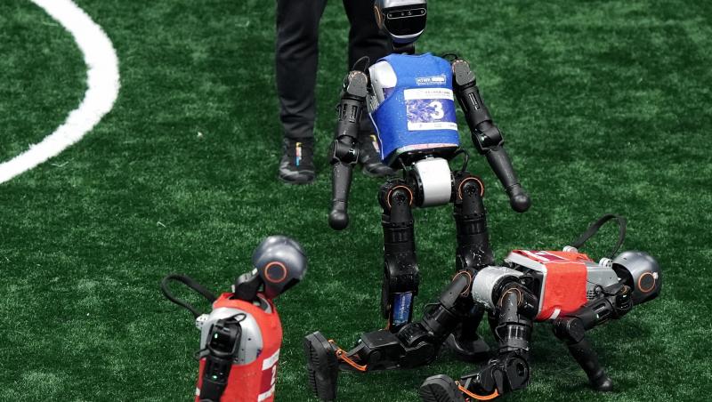 3 roboți care se află pe un teren de fotbal