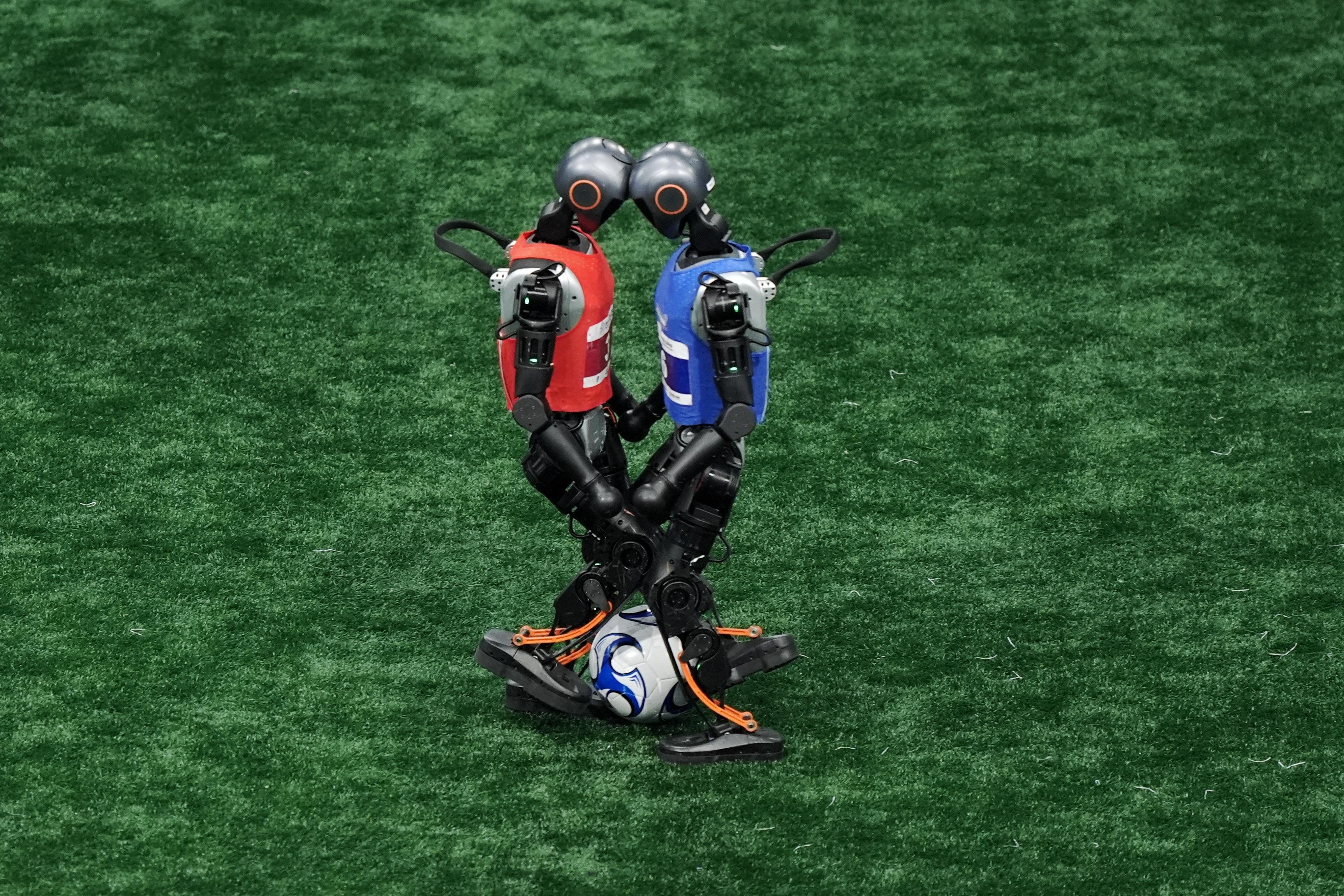 2 roboți care stau față în față pe un teren de fotbal