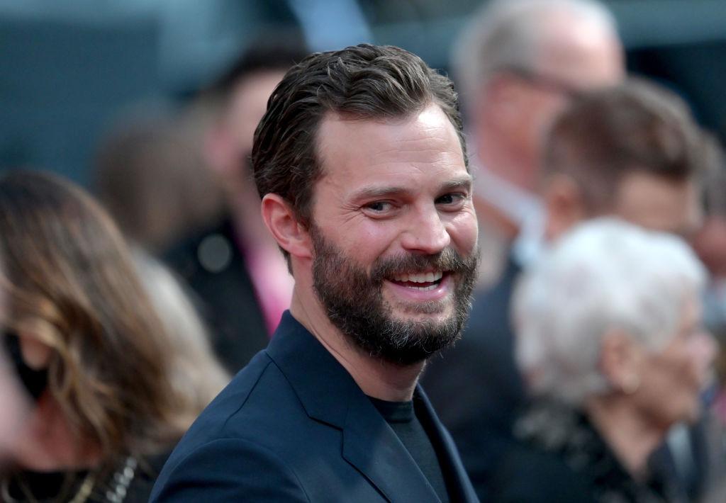 Jamie Dornan îmbrăcat cu un costum bleumarin elegant, zâmbind
