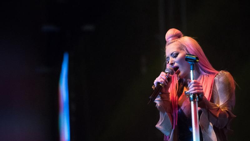 Delia îmbrăcată într-o ținută aurie cu detalii negre, cântând la microfon pe scenă