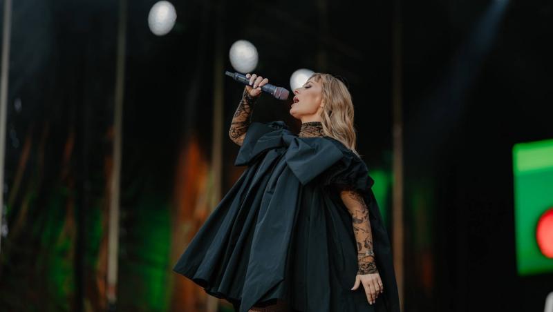 Delia îmbrăcată într-o rochie neagră extravagantă, cântând la microfon