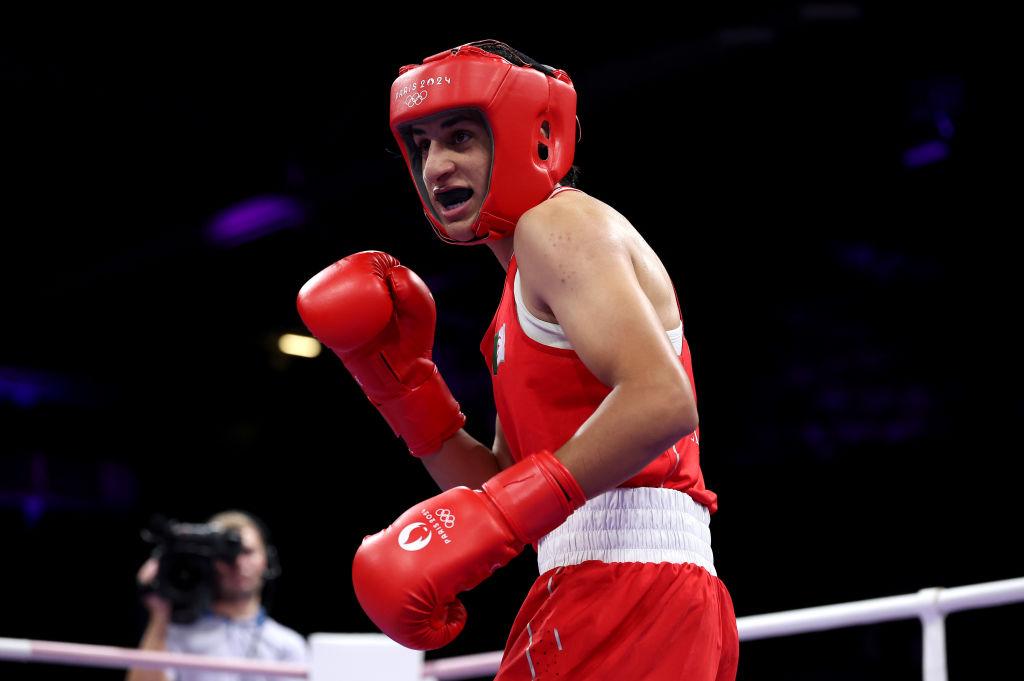 Imane Khelif îmbrăcată într-un costum de sport roșu, cu mănuși de box și cască de protecție