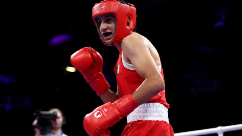 Imane Khelif îmbrăcată într-un costum de sport roșu, cu mănuși de box și cască de protecție