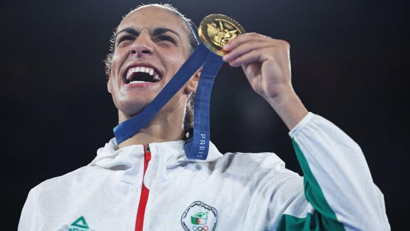 Imane Khelif îmbrăcată într-o jachetă albă cu verde, cu o medalie de aur în mână