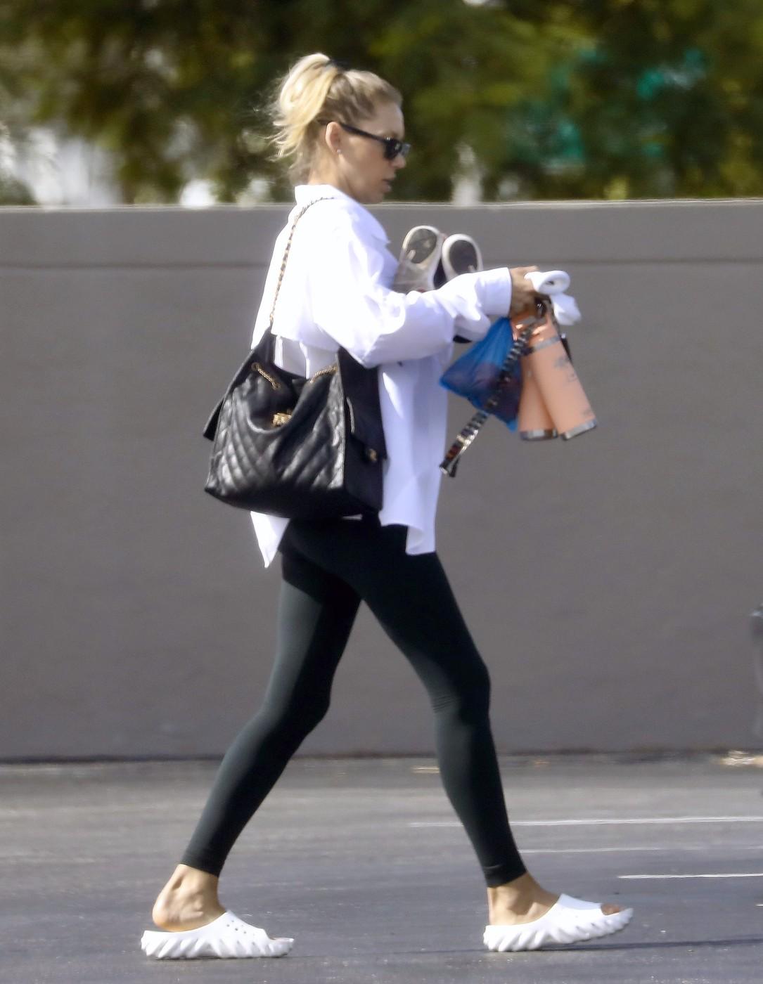 Anna Kournikova, îmbrăcată în colanți negri și cămașă albă, cu o geantă mare, neagră, pe umeri