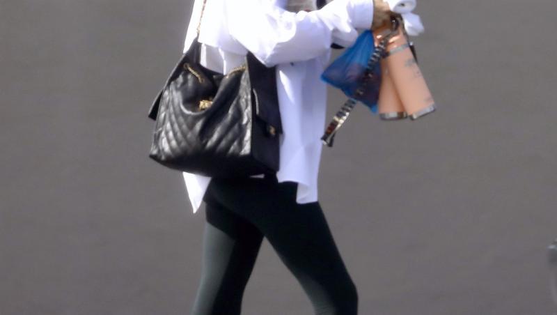 Anna Kournikova, îmbrăcată în colanți negri și cămașă albă, cu o geantă mare, neagră, pe umeri