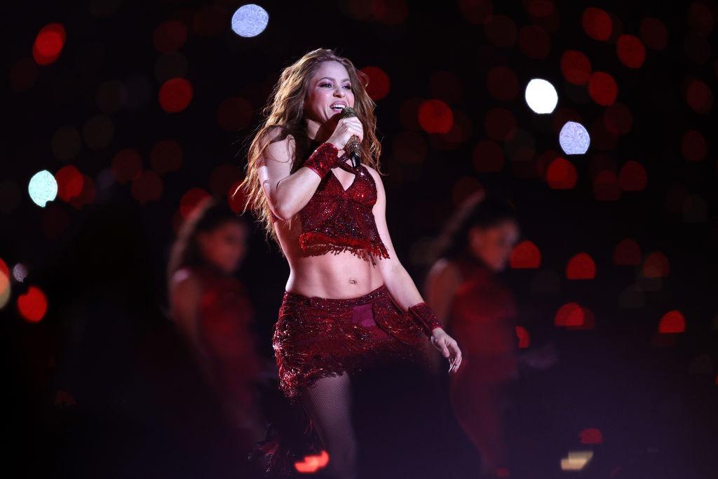Shakira pe scenă, îmbrăcată într-o ținută vișine strălucitoare