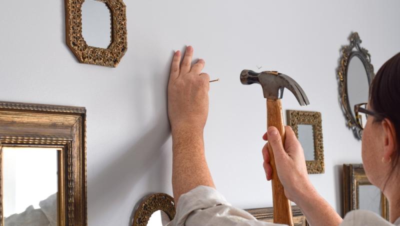femeie care bate un cui în perete unde sunt agățate mai multe oglinzi