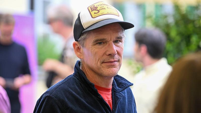 Ethan Hawke îmbrăcat cu o jachetă bleumarin peste un tricou roșu