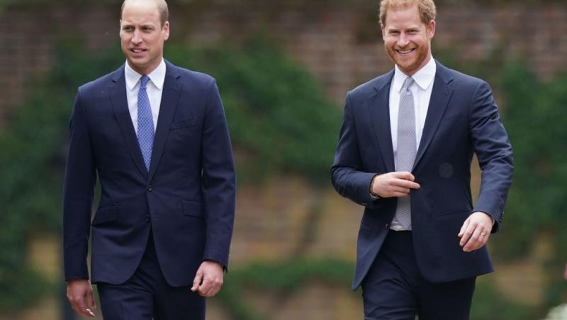 Prințul Harry și Prințul William îmbrăcați în costume bleumarin, mergând