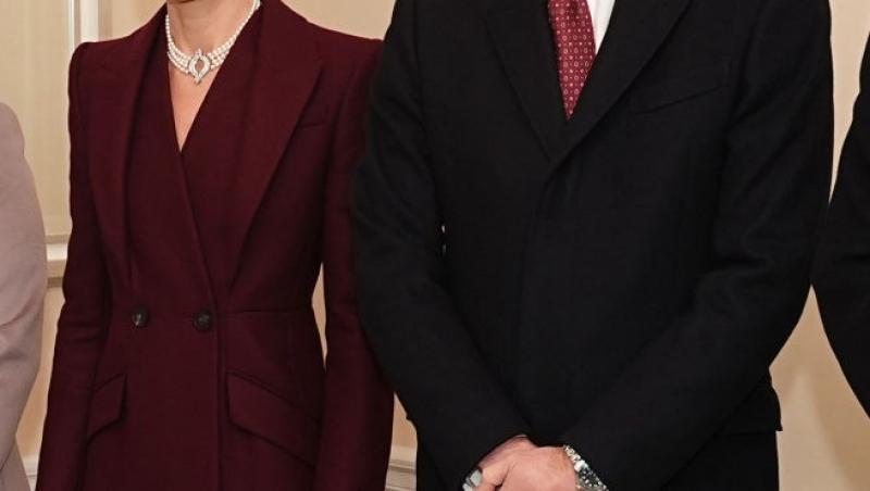 Prințul William îmbrăcat într-un costum negru, alături de Prințesa Kate, îmbrăcată într-o rochie vișinie